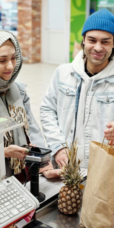A smiling couple using a smartphone to pay at a supermarket checkout counter.