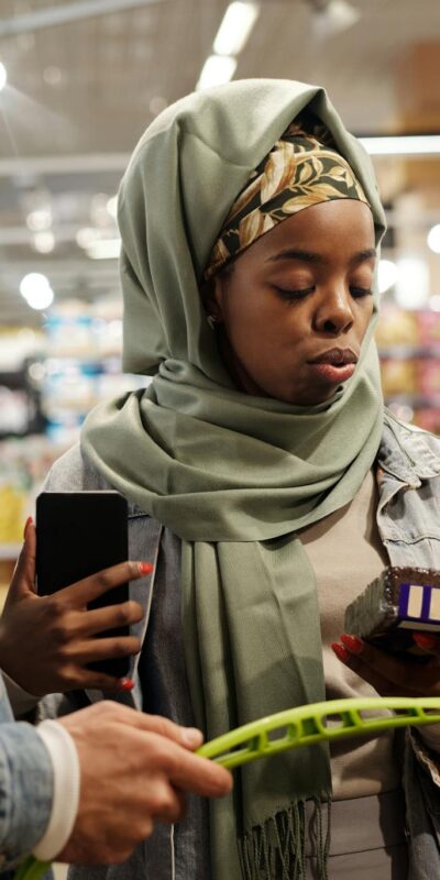 A young couple shops for groceries in a supermarket, checking items with a smartphone.