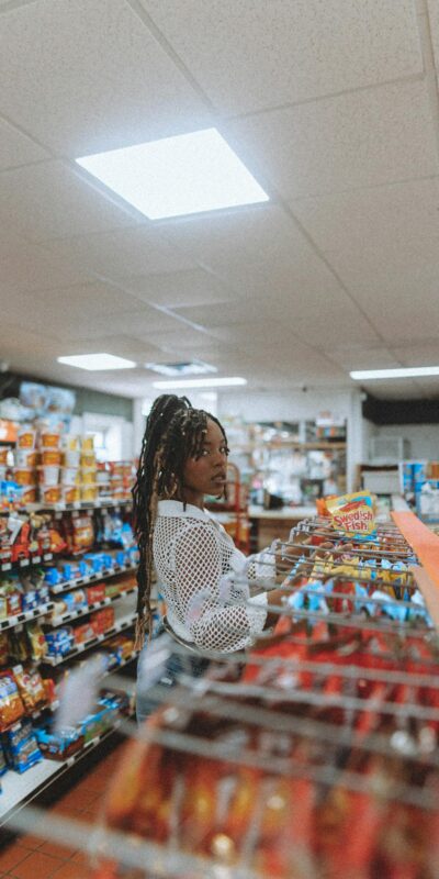 African American woman standing in a grocery store aisle, picking snacks. Indoor retail scene.
