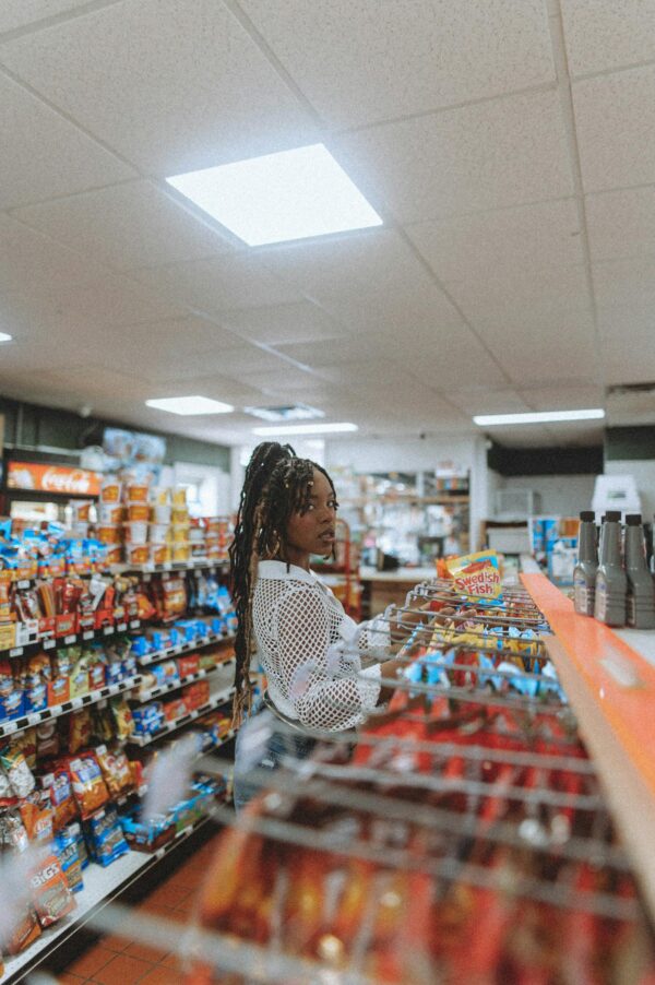 African American woman standing in a grocery store aisle, picking snacks. Indoor retail scene.