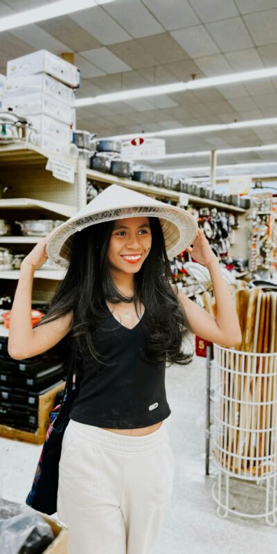 Smiling woman wearing a conical hat in a Dallas supermarket, enjoying shopping.